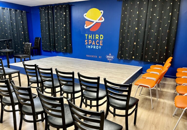 The stage with black chairs in front, orange chairs on the side, a ramp on the other side, and the logo behindi it on the wall